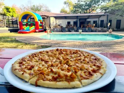 a pizza on a plate on a table near a pool at Mabalel in Crocodile Valley Estates
