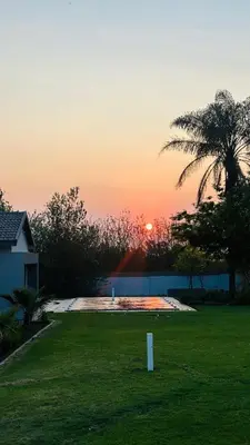 a sunset in a yard with a palm tree at Thandekile Garden Venue in Midrand