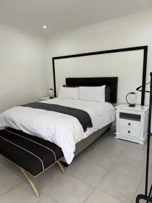 a white bedroom with a large bed and a white table at Thandekile Garden Venue in Midrand