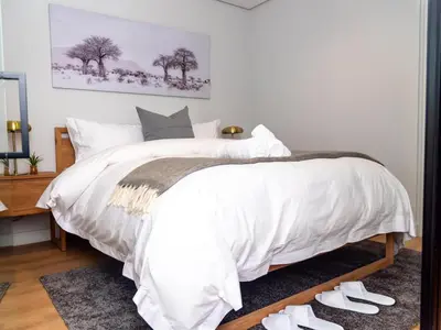 a bedroom with a bed with white sheets and white shoes at Luxurious Apartment, Ellipse, Waterfall, Midrand in Midrand