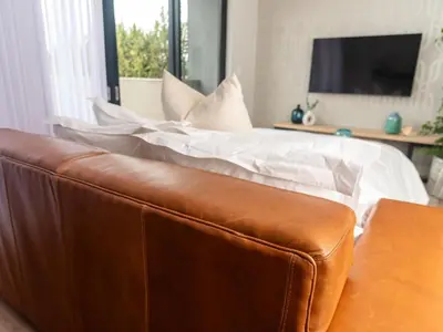 a bed with white sheets and a brown leather couch at Luxurious Apartment, Ellipse, Waterfall, Midrand in Midrand