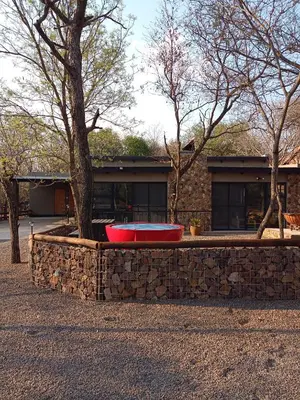 a red tub in a stone wall next to a tree at Woodpecker Villa Guesthouse in Thabazimbi