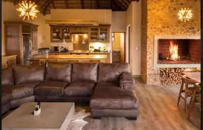 a living room with a leather couch and a fireplace at Kudu Lodge in Kromdraai