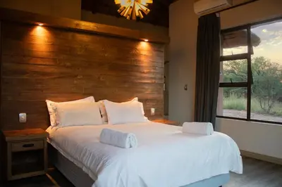 a bedroom with a large white bed with a wooden wall at Kudu Lodge in Kromdraai