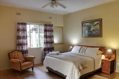 a bedroom with a bed and a chair and a window at Oppi Plaas in Hazyview