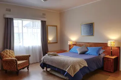 a bedroom with a bed and a chair and a window at Oppi Plaas in Hazyview