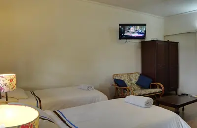 a room with two beds and a chair and a tv at Oppi Plaas in Hazyview