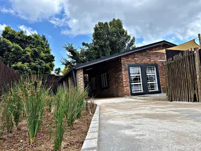 a brick house with a fence next to a driveway at Lincoln Moon Guesthouse in Graskop