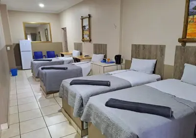 a room with four beds in a room with a kitchen at Sleep 'n Go Guesthouse in Mokopane