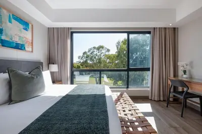 a bedroom with a bed and a desk and a large window at STAY Menlyn in Pretoria