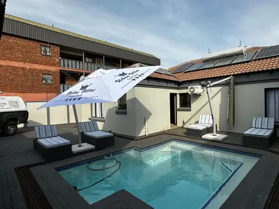 a swimming pool with an umbrella and two chairs at Urban Villas Guest House in Pretoria