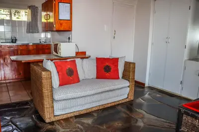 a wicker couch with red pillows in a kitchen at Panorama Chalets & Rest Camp in Graskop