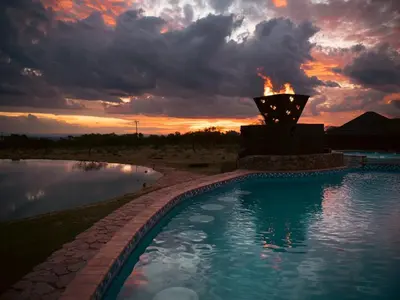 a swimming pool with a fire fountain at sunset at Shekinah Lion & Game Lodge in Dryfsand