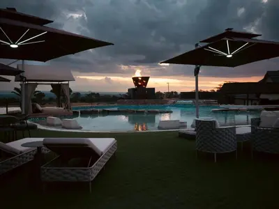 a pool with chairs and umbrellas with a sunset in the background at Shekinah Lion & Game Lodge in Dryfsand