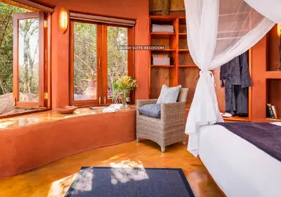 a bedroom with a bed and a chair and windows at Leshiba Wilderness in Louis Trichardt