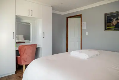 a white bedroom with a bed and a chair at Log Cabin Moonlight Meadows Dullstroom. in Dullstroom