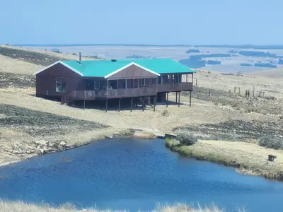 a house on top of a hill next to a river at Log Cabin Moonlight Meadows Dullstroom. in Dullstroom