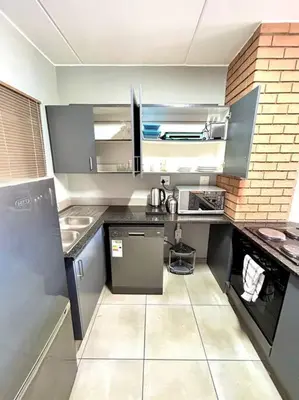 a small kitchen with black counters and appliances at The Place @ Mall of Africa in Midrand