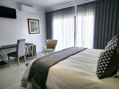 a bedroom with a bed and a desk and a window at La Chambre Manor House in Nelspruit