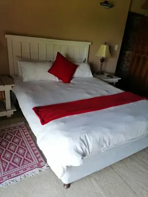 a large white bed with a red blanket on it at Kwena Maribane Lodge in Erasmus