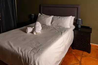 a bed with white sheets and pillows next to a night stand at Harties Lodge - Bay View 5 in Hartbeespoort