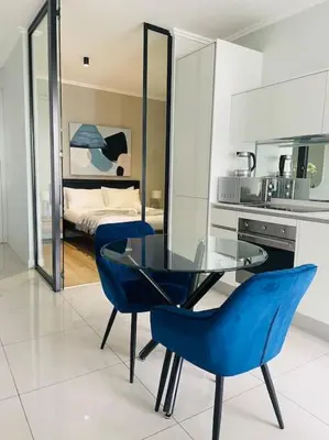 a glass table and two blue chairs in a kitchen at Ellipse Waterfall Luxury Apartment in Midrand