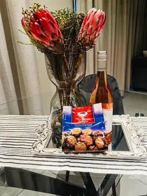 a glass table with a bottle of wine and flowers at The Comfort AirB&B - On the 8th floor luxury 1 bedroom apartment with views in Pretoria