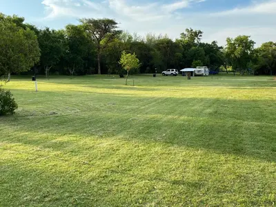 a large grass field with a car parked in the background at De Rust Campsite in Hammanskraal