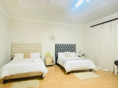 two beds in a bedroom with white walls and wood floors at Tuscany Guesthouse in Midrand
