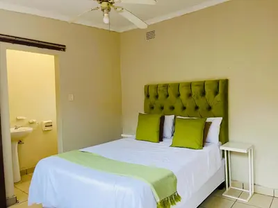 a bedroom with a large bed with green pillows at Genesis Guesthouze in Bela-Bela