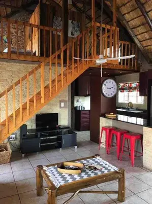 a living room with a staircase and tables and a clock at Kudu's Rus in Marloth Park in Marloth Park