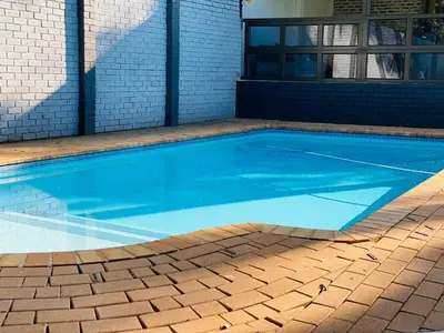 a blue swimming pool in front of a building at Bridgelamour Guest House in Hartbeespoort