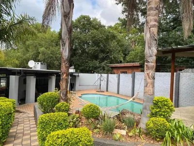 a swimming pool with a hammock between two palm trees at Bridgelamour Guest House in Hartbeespoort