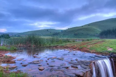 a waterfall in a field with hills in the background at Strathwold Cottages in Machadodorp