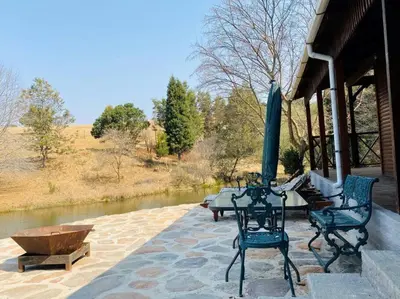 a patio with a table and chairs and a river at Strathwold Cottages in Machadodorp