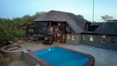 a house with a thatched roof and a swimming pool at P.A.P.E's RETREAT in Marloth Park