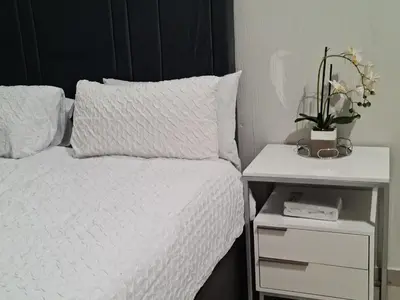 a bedroom with a white bed and a night stand with a plant at Falcon's Nest in Pretoria