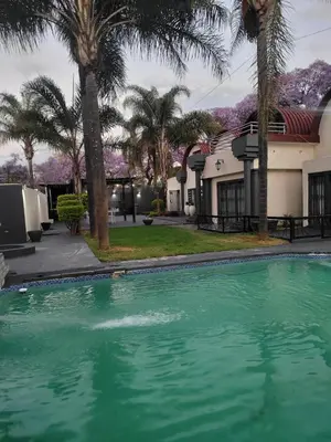 a swimming pool in front of a house with palm trees at Falcon's Nest in Pretoria