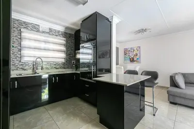 a kitchen with black cabinets and a sink and a couch at Signature Lodge in Kempton Park