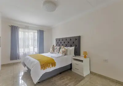a white bedroom with a large bed and a window at Signature Lodge in Kempton Park