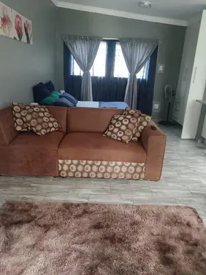 a living room with a brown couch and a bed at Protea guest house in Pretoria