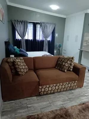 a brown couch in a living room with a bed at Protea guest house in Pretoria