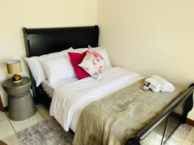 a bedroom with a bed with white sheets and red pillows at Khubonye Royal Guesthouse in Randjesfontein