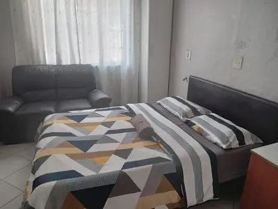 a bed with a comforter and a chair in a room at Las Palmas Day & Night Guest House in Pretoria