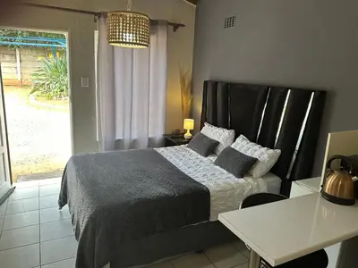 a bedroom with a bed and a table and a window at Relax in Nature Cottage Close to OR Tambo International Airport in Kempton Park