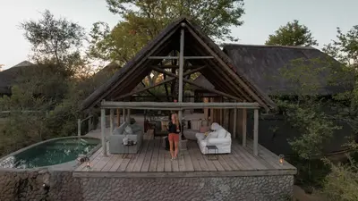 a woman standing on a deck next to a house at Nsala Wilderness Camp in Timbavati Game Reserve