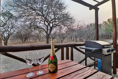a bottle of champagne sitting on a wooden table with wine glasses at Lion Den in Marloth Park