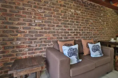 a couch against a brick wall with pillows on it at Lion Den in Marloth Park
