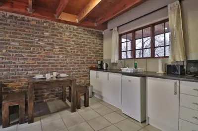 a kitchen with white cabinets and a brick wall at Lion Den in Marloth Park