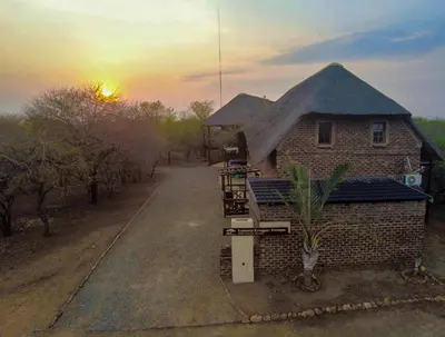 a house with a thatched roof with the sunset in the background at Leopard Chalet - Solar System in Marloth Park